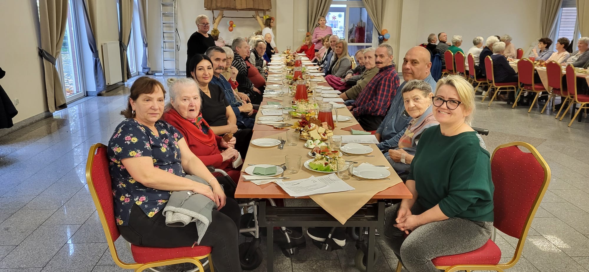 Seniorzy z DPSu wspólnie siedzą przy stole w świetlicy wiejskiej w Mojęcicach i świętują dzień seniora 