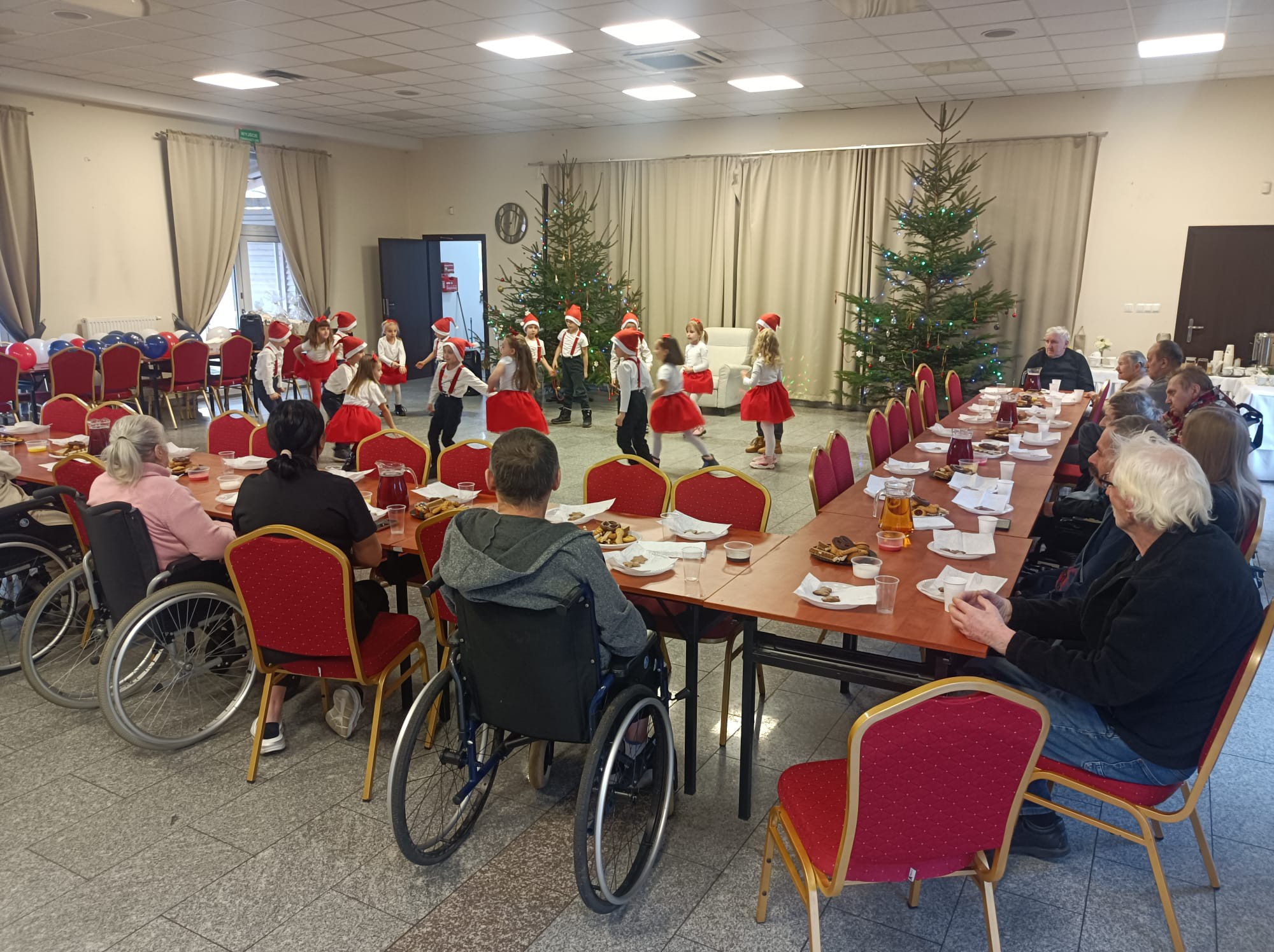 Dzieci ze szkoły podstawowej występują przed seniorami w mikołajowych czapkach