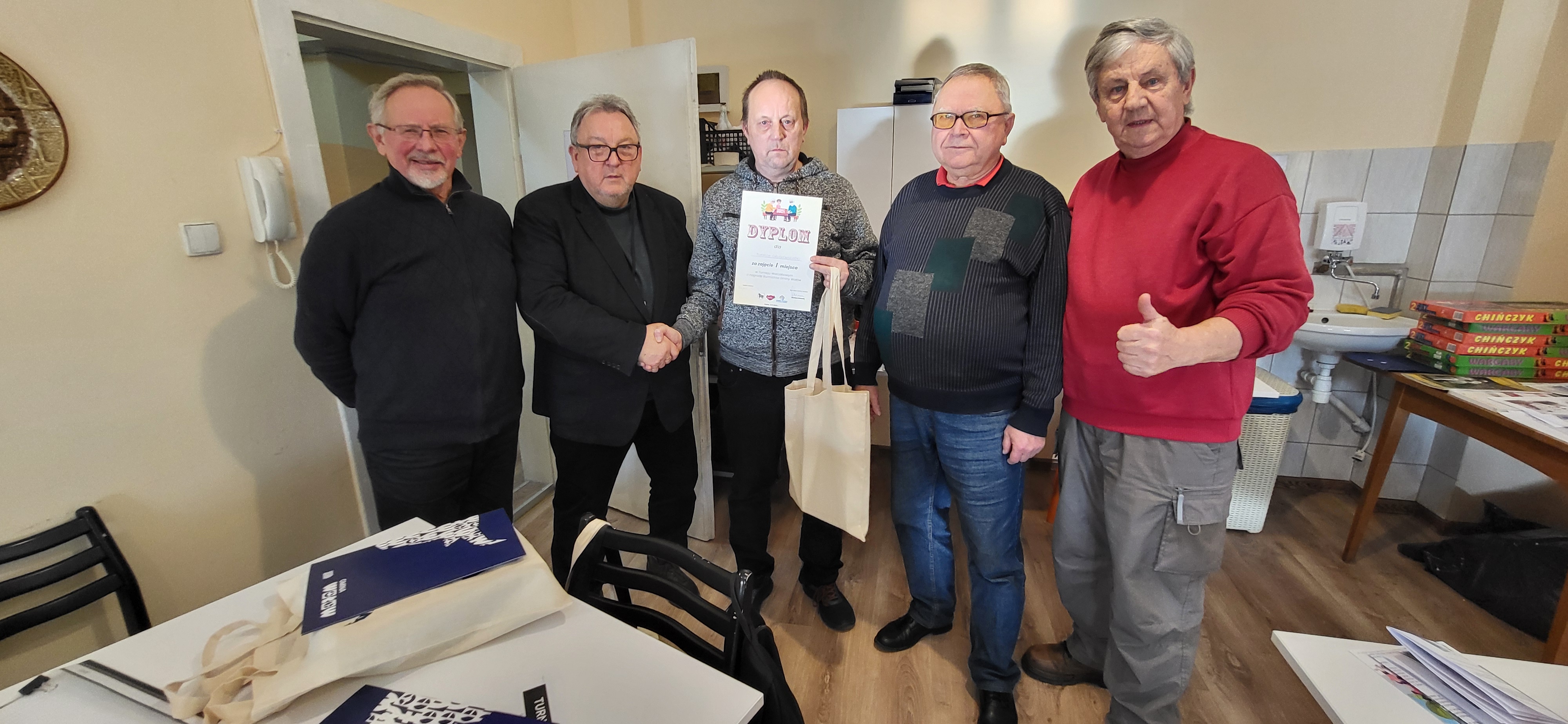 Pan Tomasz trzyma dyplom za zajęcie I miejsca w warcabach podając rękę Panu Eugeniuszowi Stańczakowi 