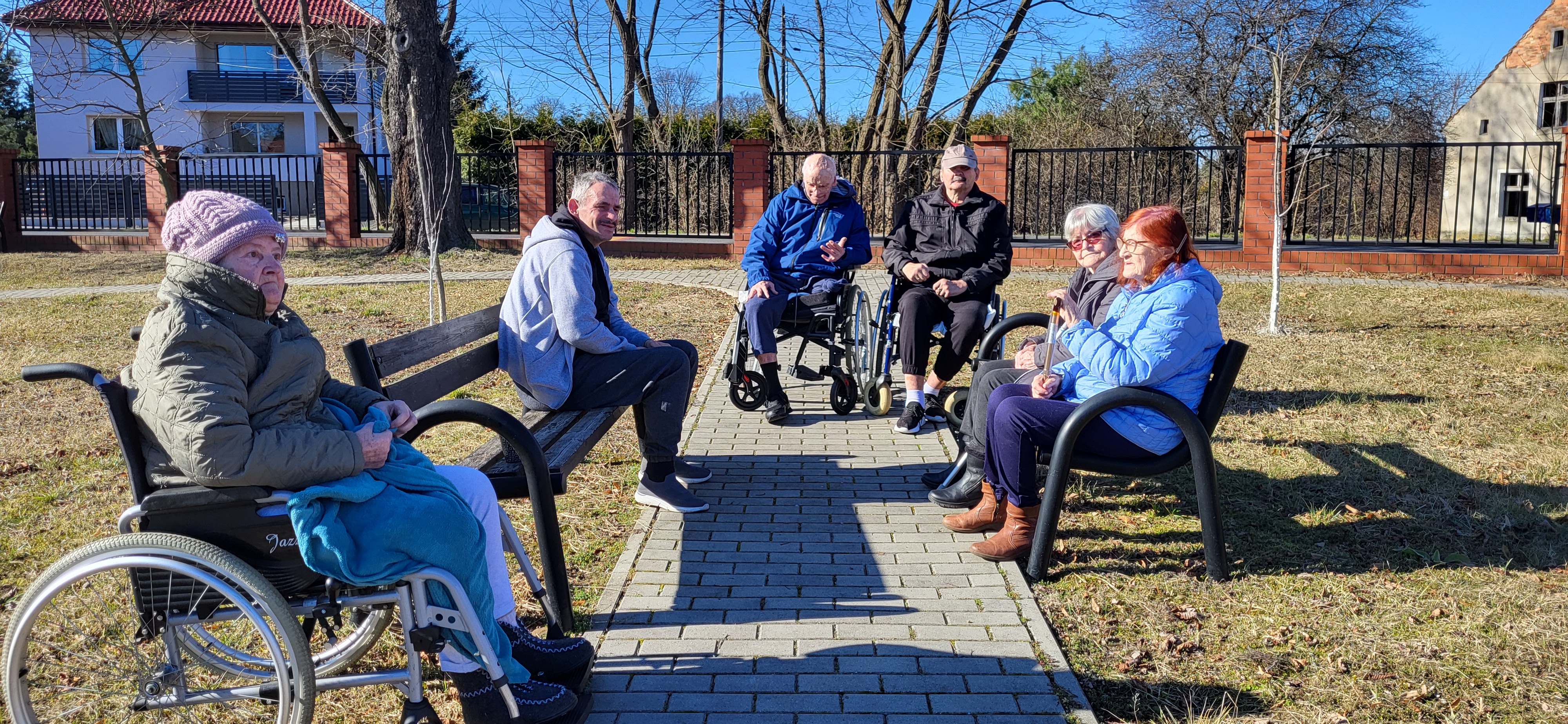 Mieszkańcy siedzą na ławce na dworze i ogrzewają się w słońcu